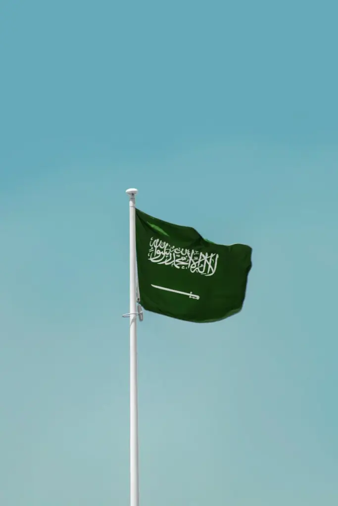 National flag of Saudi Arabia waving on a flagpole against a clear blue sky in Riyadh.