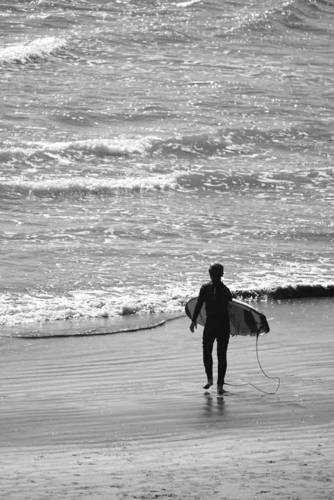 Silhouette of a surfer walking towards the ocean carrying a surfboard, capturing a peaceful beach scene.