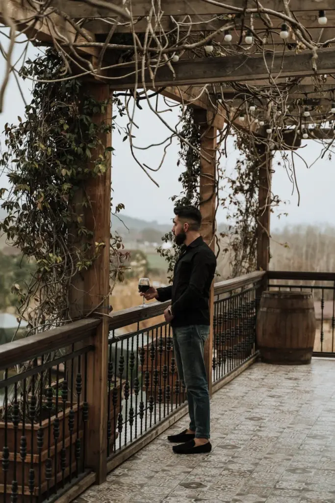 A man in casual attire enjoys a peaceful moment with red wine on a rustic terrace.