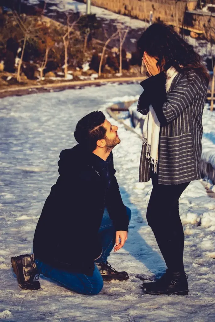 A man proposing to his girlfriend in a snowy park during winter, capturing a heartfelt moment outdoors.