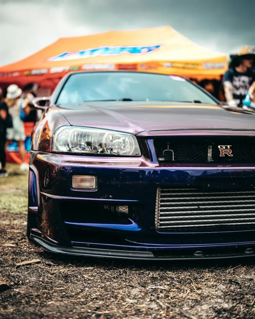 Vibrant photo of a blue Nissan GT-R sports car displayed at an outdoor event with colorful tents.