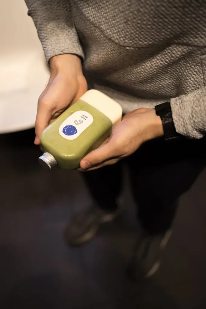 Hands holding a bottled green juice indoors in New York City, emphasizing health and wellness.