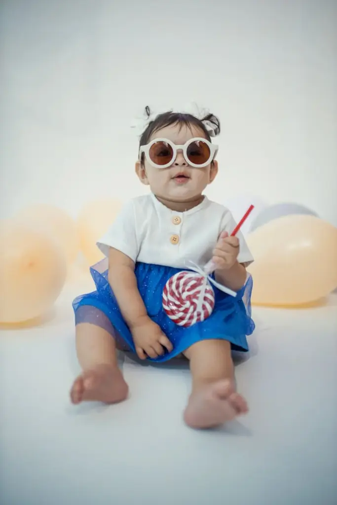 Cute baby in a blue dress with sunglasses and balloons, perfect for festive or birthday themes.
