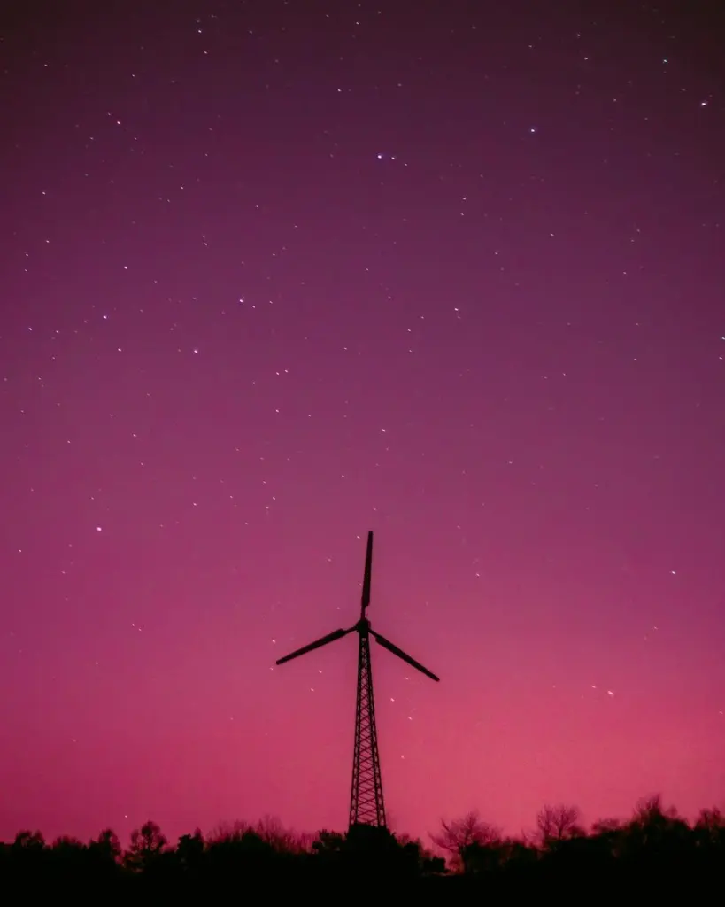 Wind turbine silhouette with a vibrant purple sky and stars, symbolizing renewable energy.