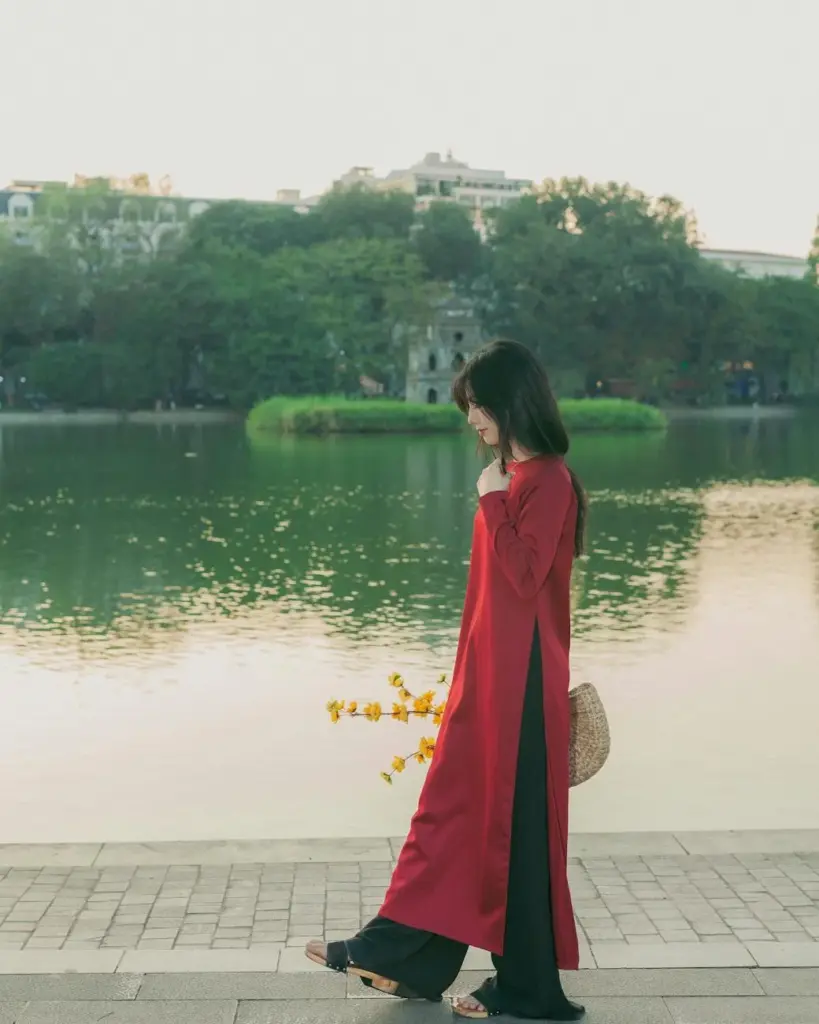 Woman wearing red ao dai walking by Hanoi's Hoan Kiem Lake, Vietnam.