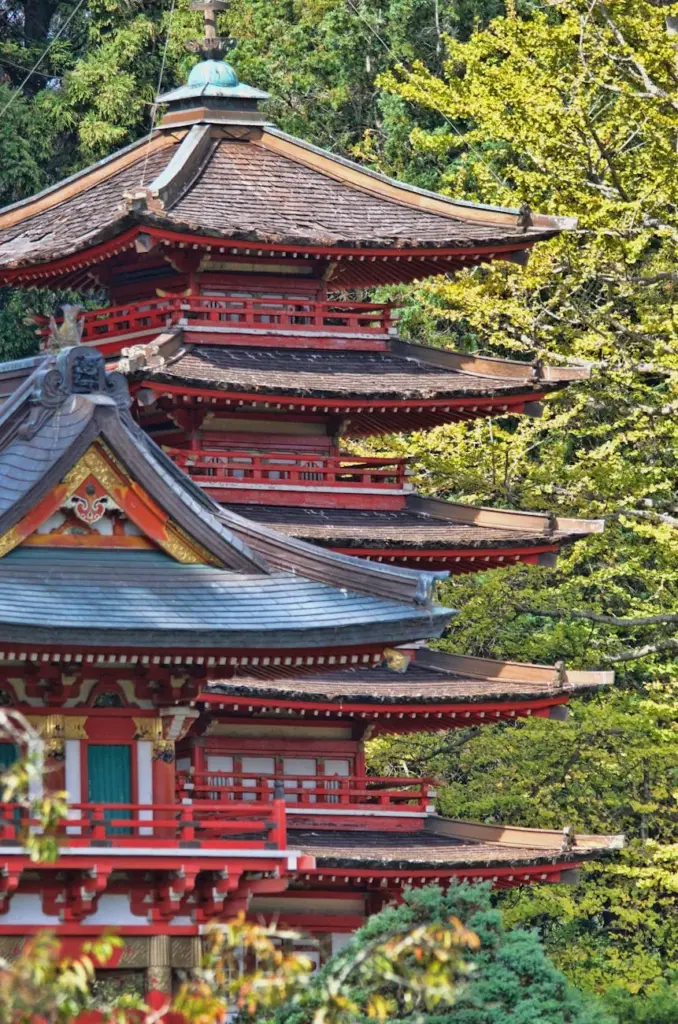 A stunning red wooden pagoda surrounded by lush green trees in spring, showcasing traditional Japanese architecture.
