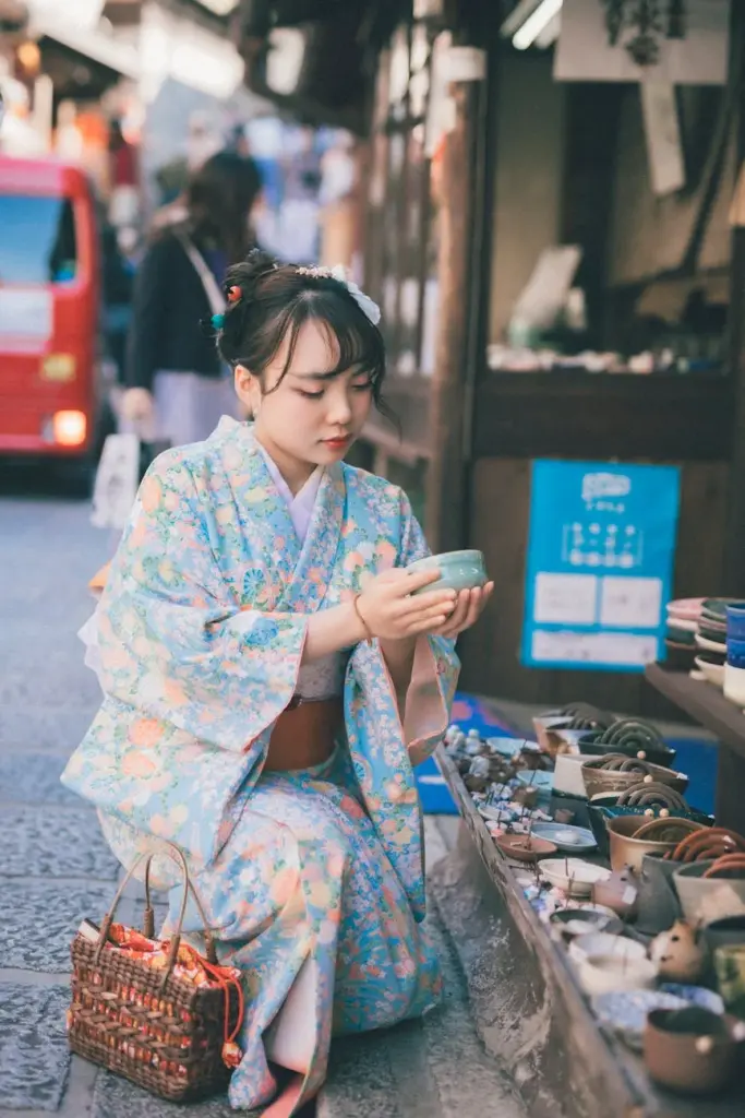 A Japanese woman wearing a kimono selects pottery in a traditional shop.