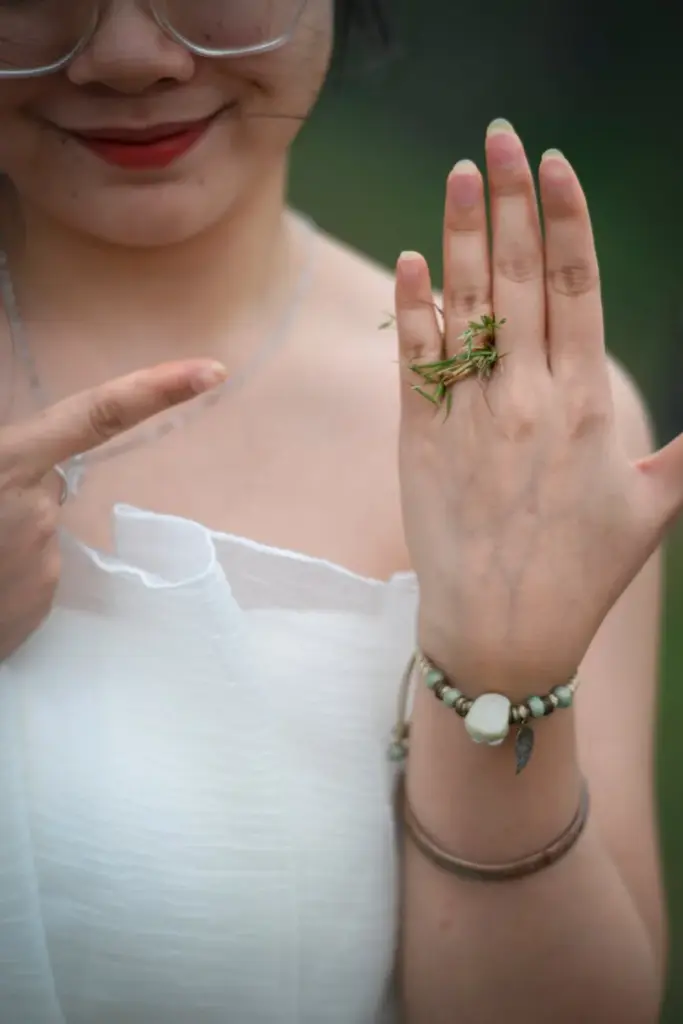 Close-up of a young woman showing a grasshopper on her hand outdoors in Vietnam.