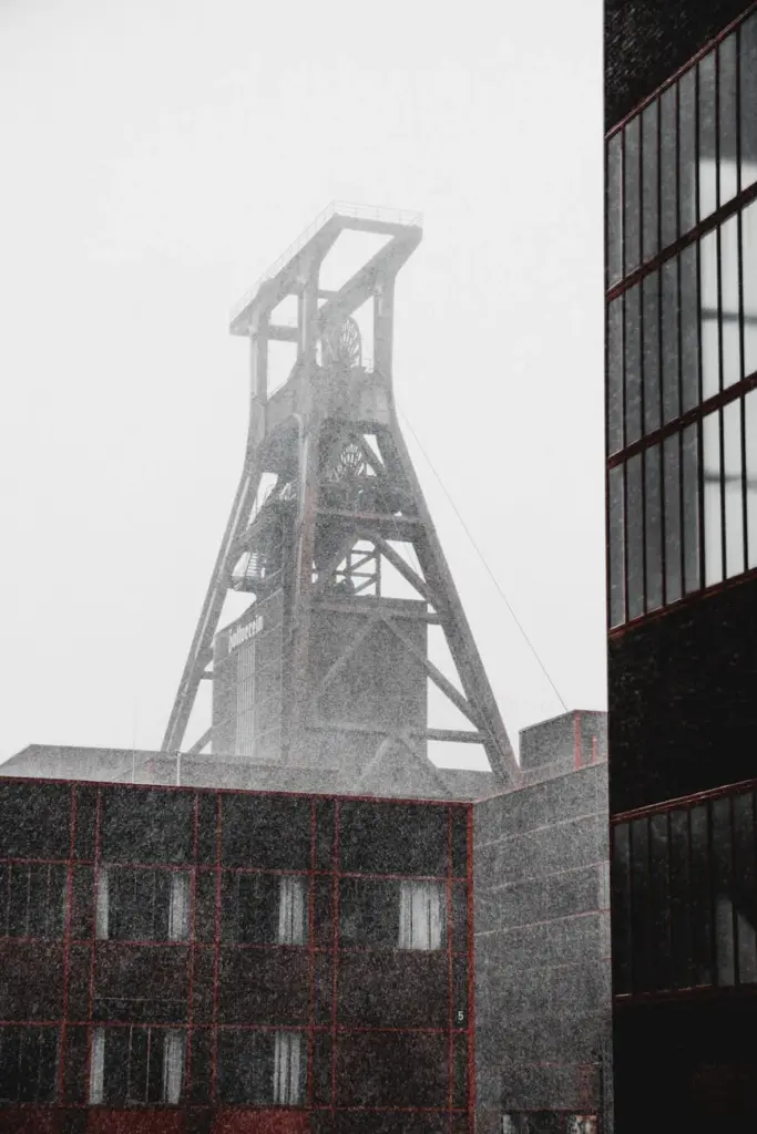 Snow falls on the historic Zollverein coal mine in Essen, showcasing industrial architecture in monochrome.