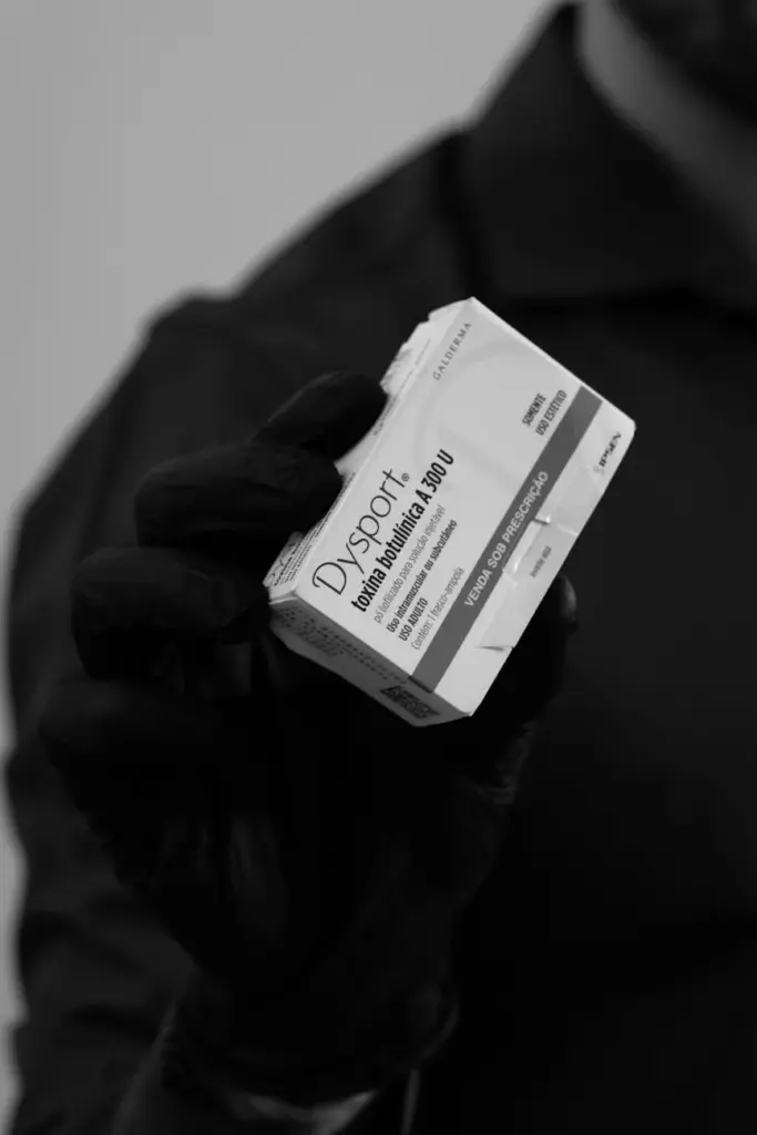 Black and white photo of a person holding Dysport packaging in a gloved hand.