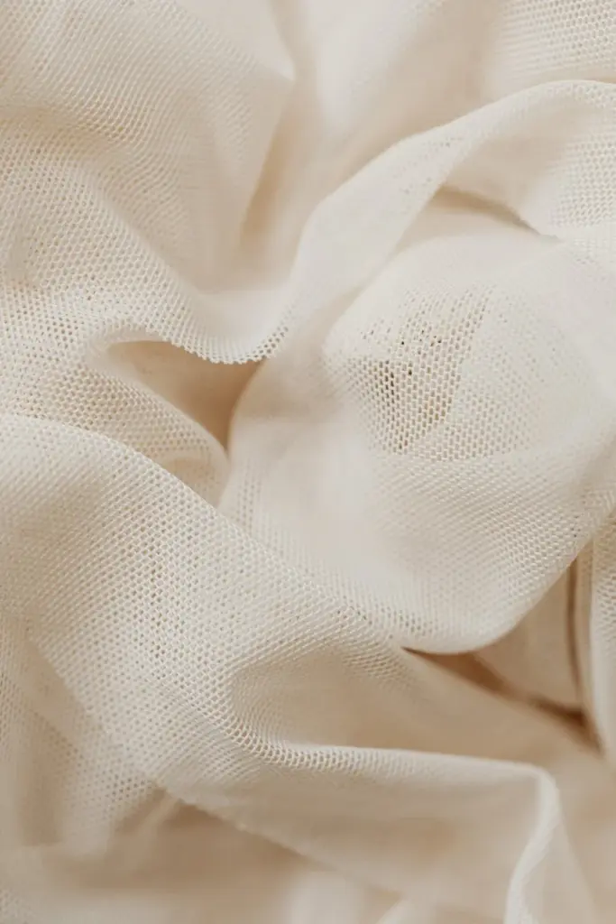 Detailed texture of beige sheer fabric with elegant folds, perfect for textile projects.