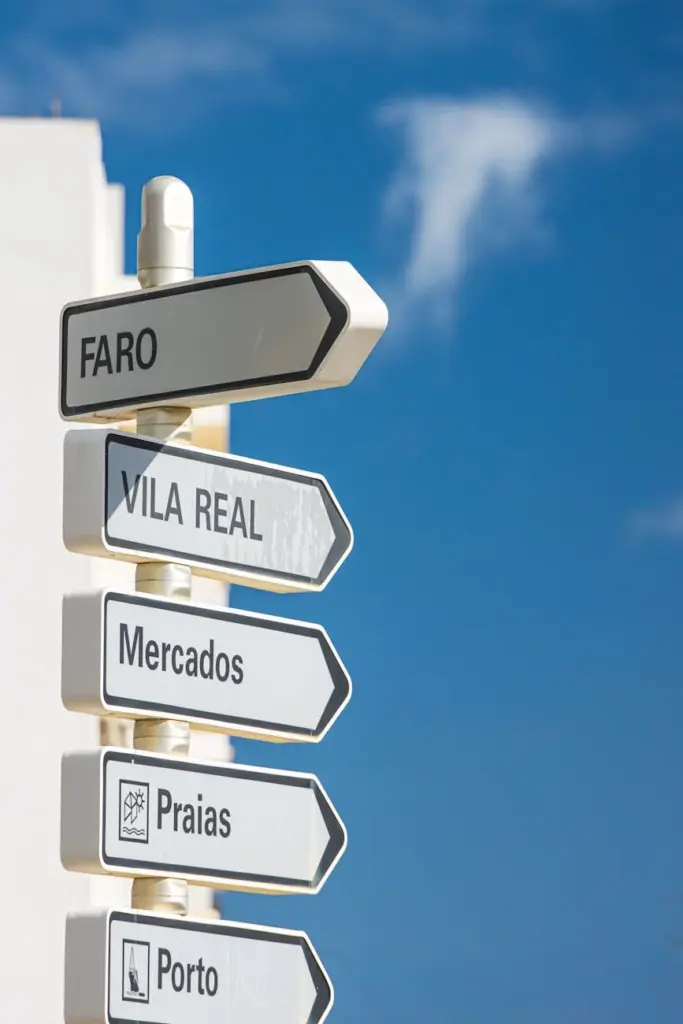 Street signpost in Olhão pointing to Faro, Vila Real, and Porto under a clear blue sky.