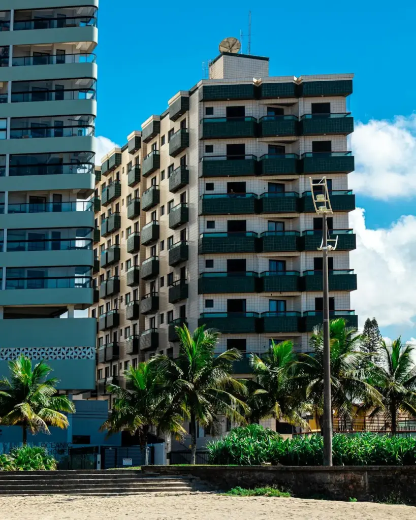 Contemporary beachfront apartments in Praia Grande, São Paulo, surrounded by palm trees and clear blue skies.