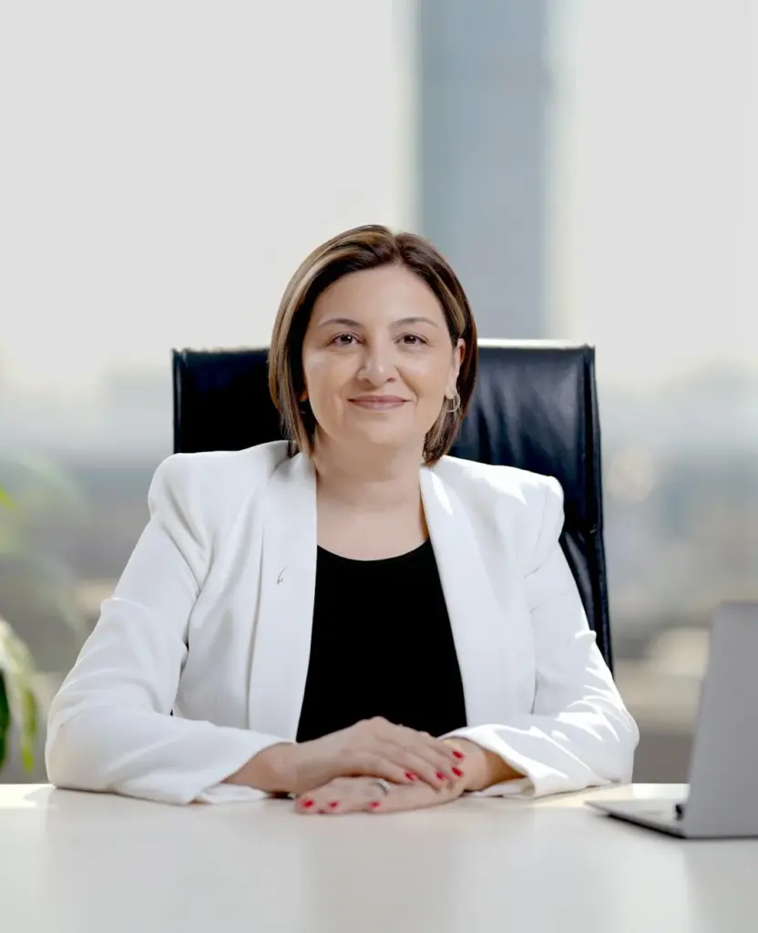 Smiling businesswoman in white blazer at desk, exuding confidence in corporate office.