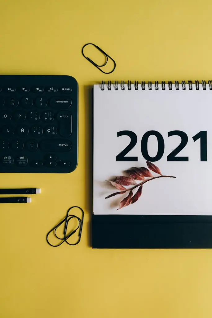 Top view of a 2021 calendar with fall leaves on a yellow background, featuring a keyboard and stationery.