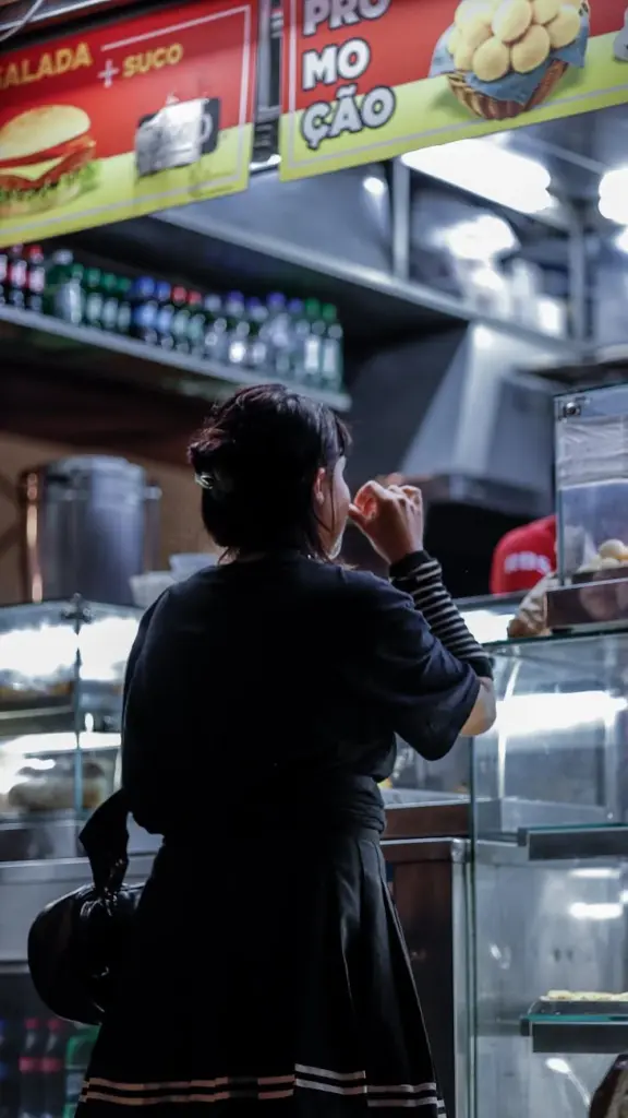 A woman ordering food at a vibrant street food stall in São Paulo, Brazil, at night.
