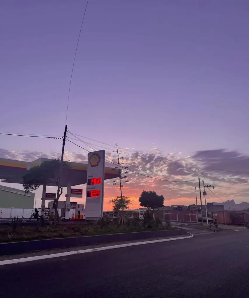 A Shell gas station under a vibrant sunset in a Cabo Verde town, highlighting urban life.