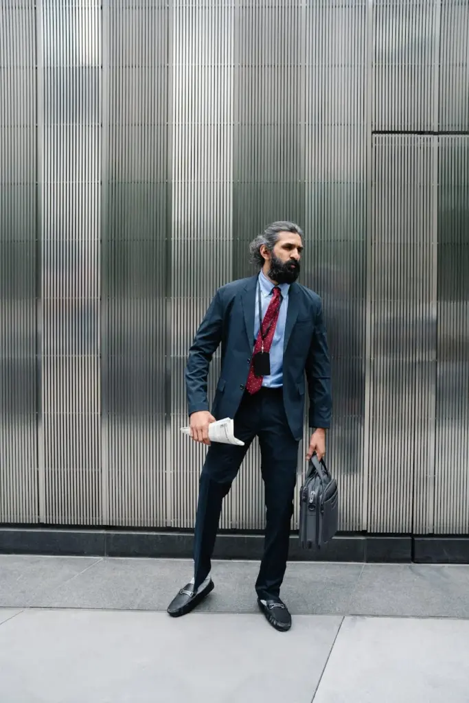 Professional businessman in formal attire with briefcase against modern building exterior.