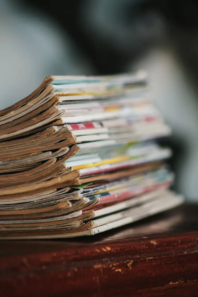 Close-up of a stack of worn magazines on a wooden table with a blurred background.