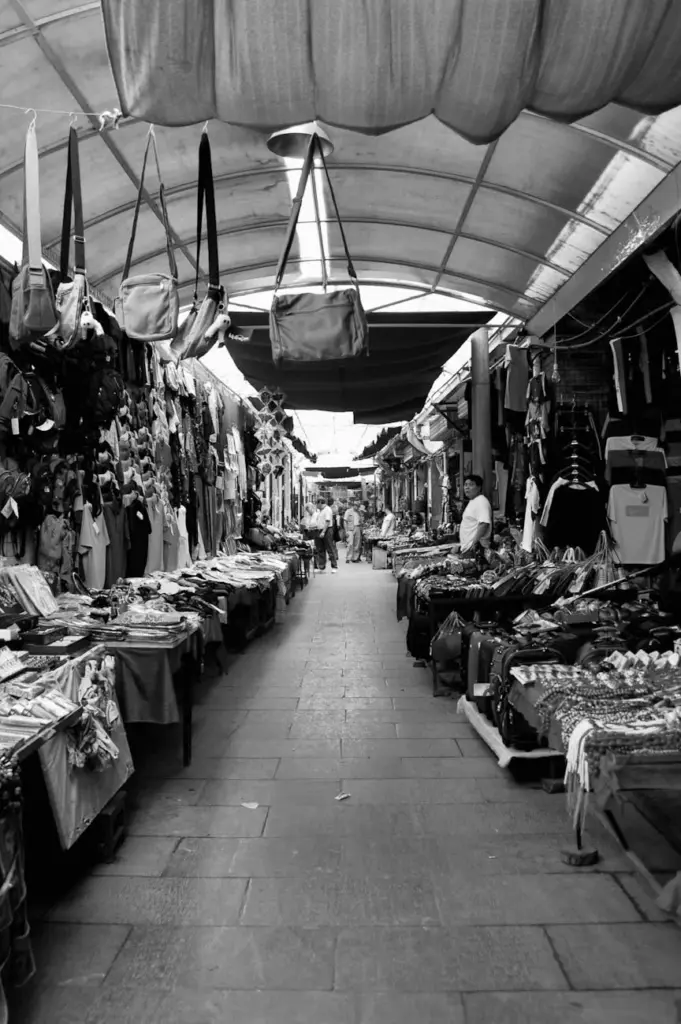 Lively black and white photo of an indoor street market with various goods.