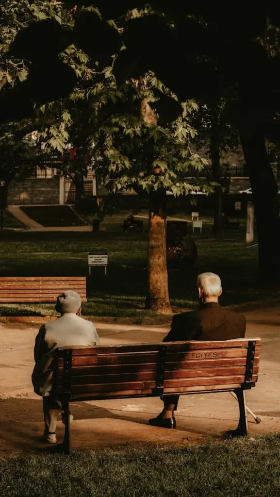 Senior couple sitting on a park bench, enjoying a serene summer afternoon outdoors.