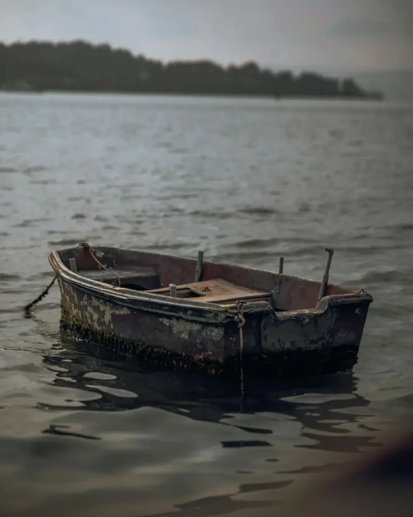An old wooden boat gently floats, moored on calm waters with a serene horizon.