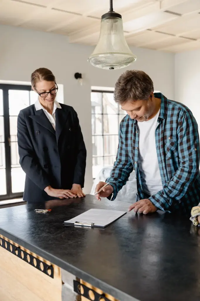 A businesswoman guides a homeowner through property signing at a kitchen counter.