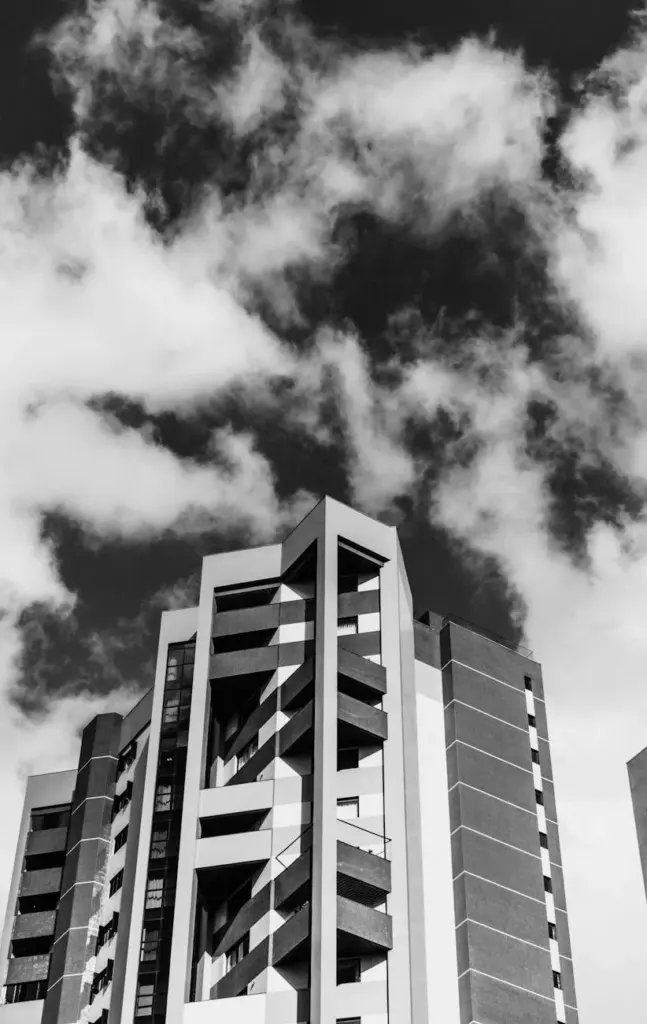 Black and white photo of a modern building with dynamic clouds in the sky.