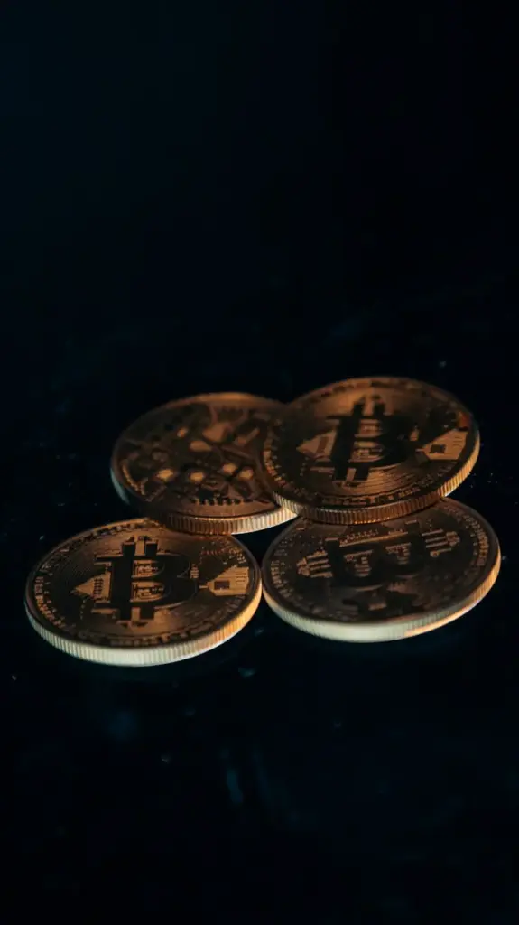 Four gold-colored Bitcoin coins arranged on a dark surface.
