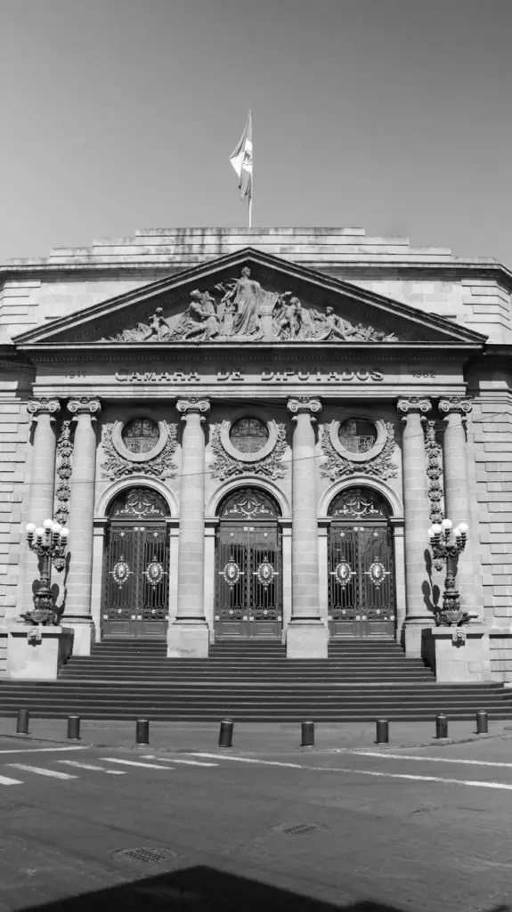 Black and white photo of a historic government building with columns and sculptures in Mexico City.