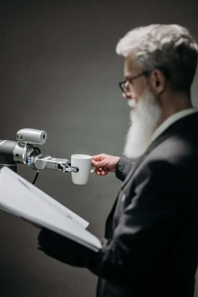 Elderly man interacts with robot arm holding a cup, showcasing innovation indoors.