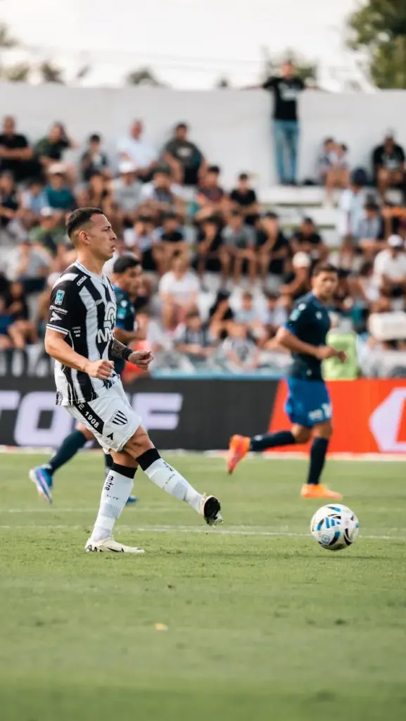 Dynamic scene of players during a competitive soccer match on a sunny day with a crowd in the background.