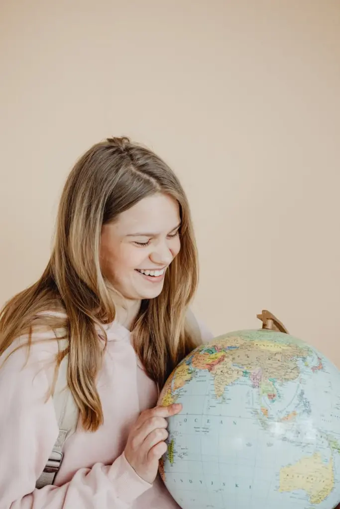 Teenage girl smiling while holding a globe against a neutral beige background.