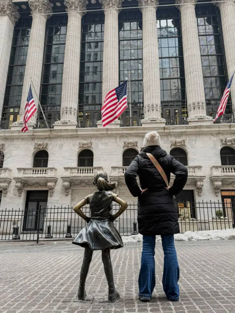 Fearless Girl statue with an adult in front of New York Stock Exchange, Wall Street, NYC.