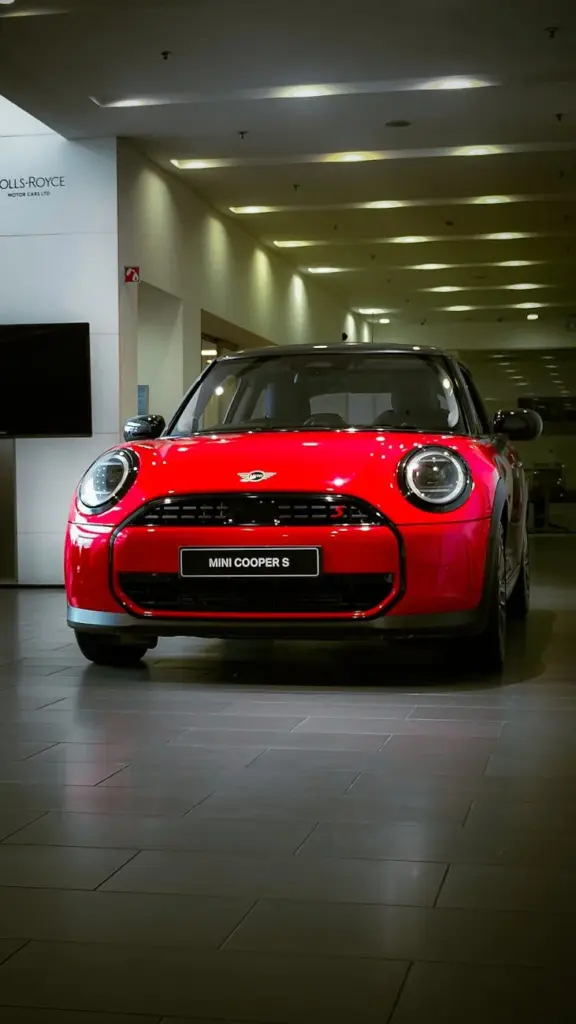 Vibrant red Mini Cooper S displayed in a sleek, modern car showroom with bright overhead lighting.