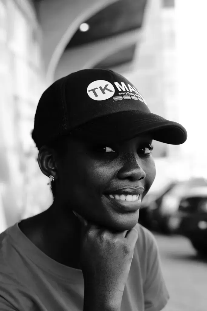 Black and white photo of a smiling woman wearing a cap with arches in the background.