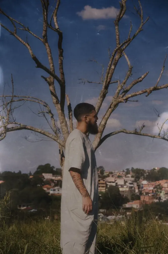 A bearded man stands thoughtfully in front of a tree in São Paulo's countryside.