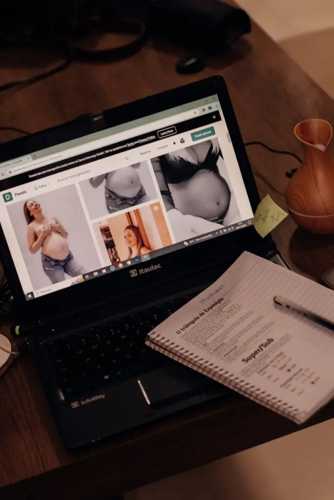 A laptop displaying pregnancy photos next to a notebook on a wooden desk, creating a warm and cozy work environment.