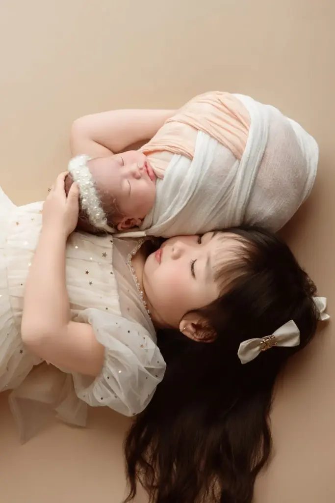 A peaceful studio portrait of a newborn baby and a child sibling sharing a tender moment.