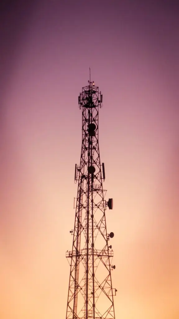 Dramatic silhouette of a telecommunication tower against a vibrant sunset sky in Adrar, Algeria.
