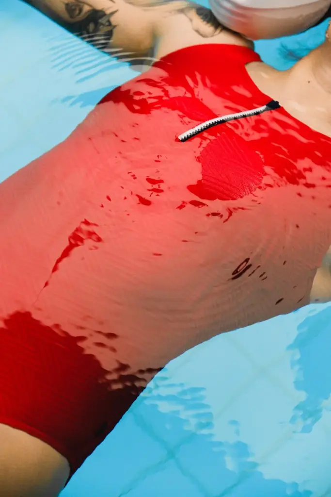Close-up of a person floating in a pool wearing a red swimsuit with a zipper.