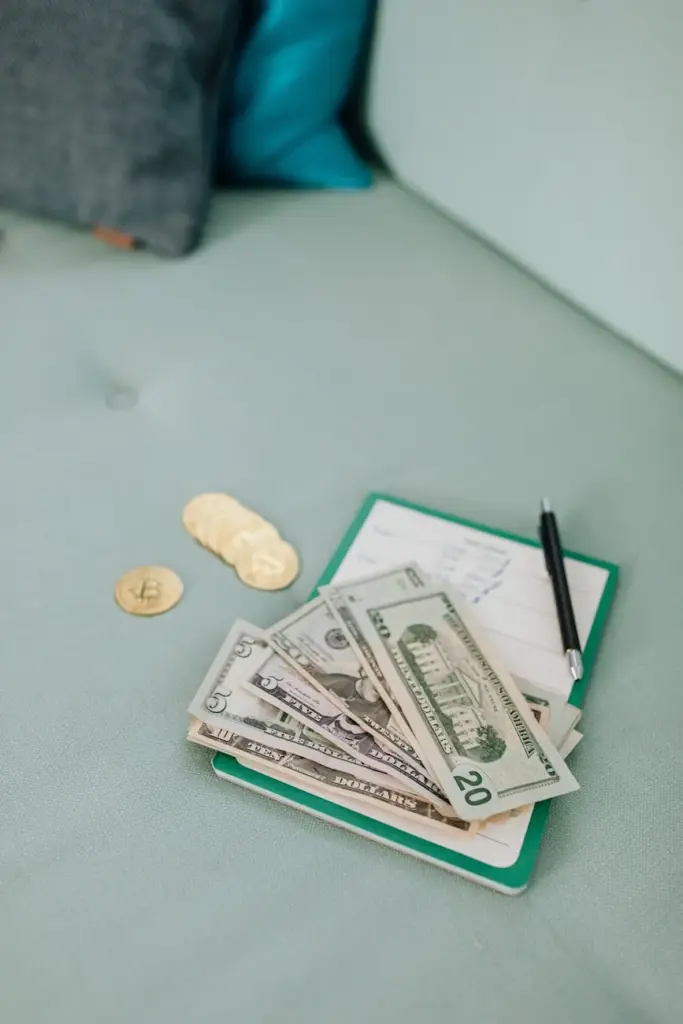 A close-up of US dollar bills and cryptocurrency coins on a notebook with a pen.