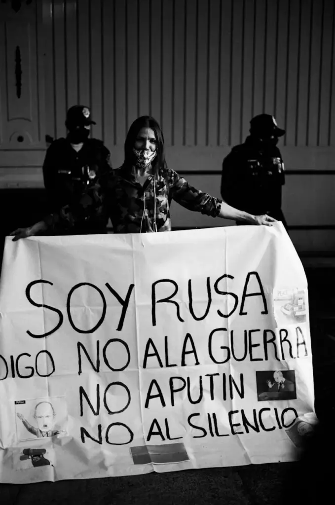 A woman holding an anti-war banner during a protest with police officers in the background.