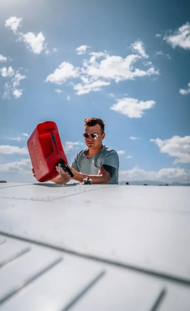 Stylish young male aviator in casual clothes and sunglasses pouring petrol from red canister into airplane tank before departure on sunny day