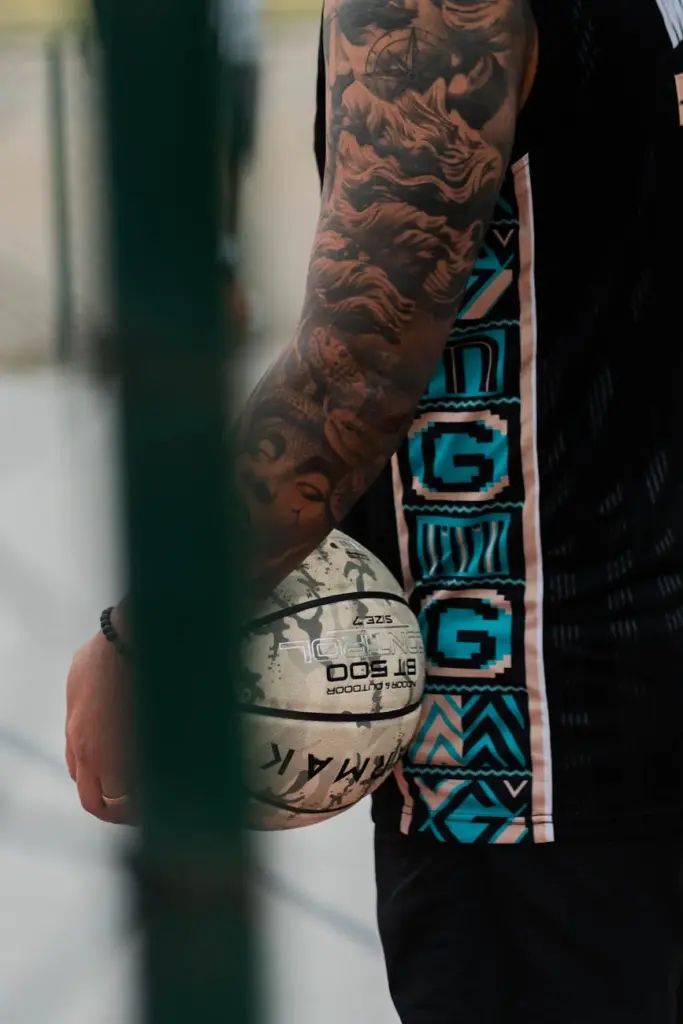 Close-up of a tattooed arm holding a basketball outdoors, emphasizing the unique tattoo design.