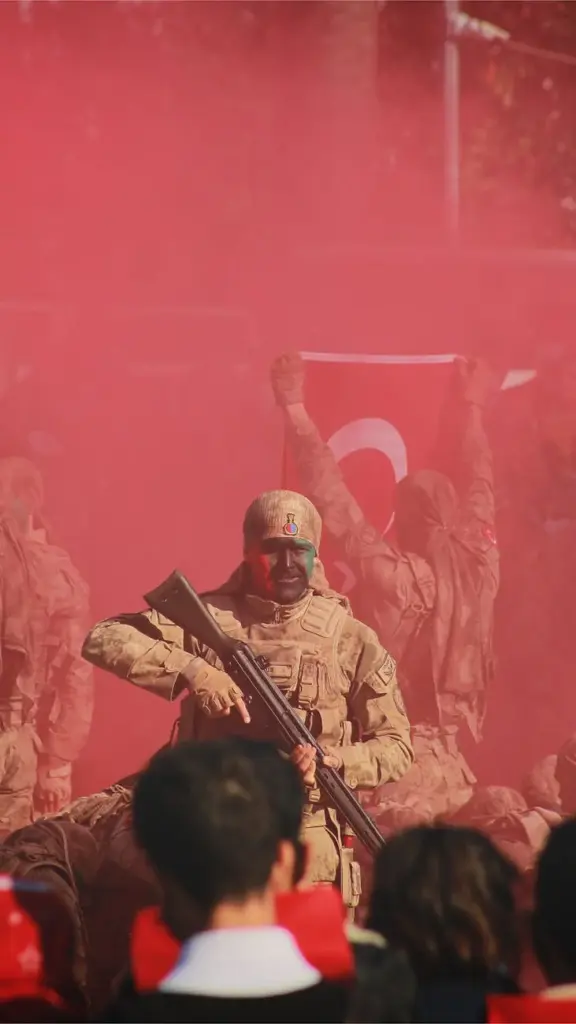 Soldier holding rifle in red smoke with Turkish flag in background at military event.