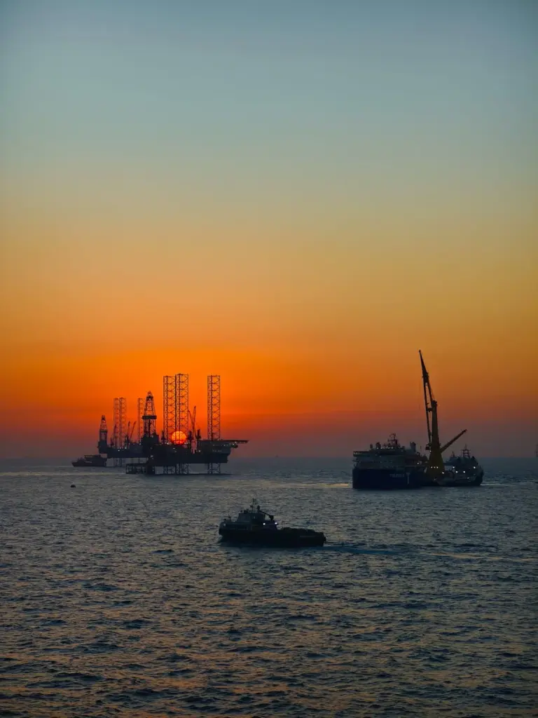 Silhouetted offshore oil rigs and boats during a vibrant ocean sunset.
