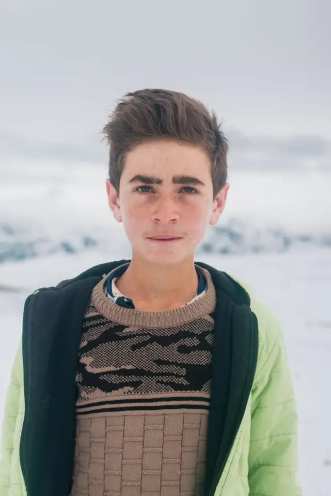 A close-up portrait of a young boy standing in snowy Kars, Türkiye.