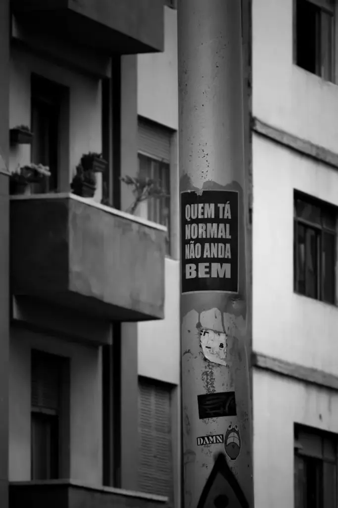 Black and white photo of a street light pole with an inspirational sticker in a city setting.