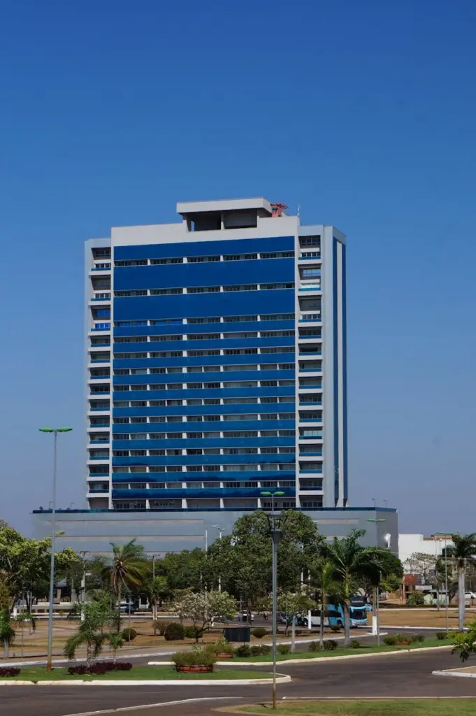 Contemporary high rise building with glass walls located on street with lush green trees against blue sky in city on summer day
